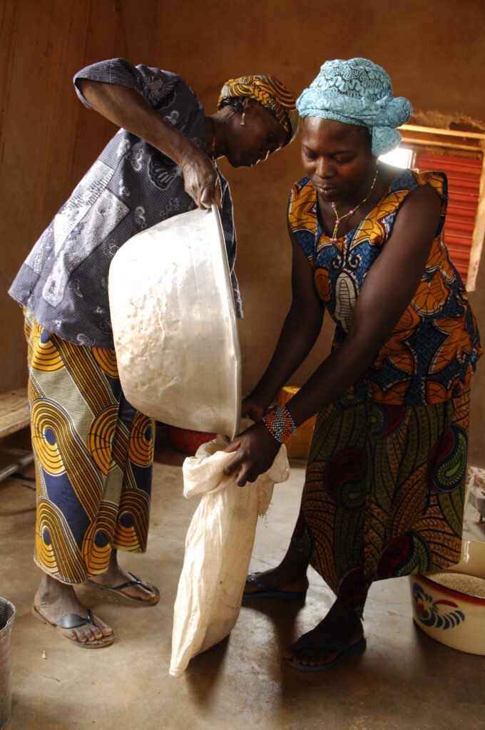 Paysan et paysanne qui versent des céréales dans un sac dans un grenier alimentaire au Burkina Faso