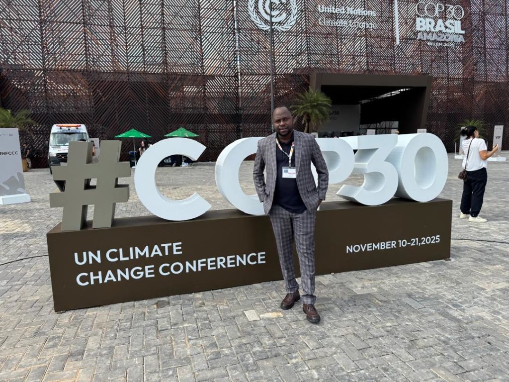 Un homme d'origine africaine posant devant un bâtiment avec une signalétique COP 30