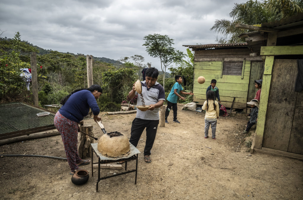 Une famille de caféiculteurs entrain de toaster le café dans la cour de leur maison avec leurs enfants jouant au ballon